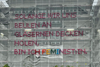 Das handbestickte Baustellennetz der Künstlerin Katharina Cibulka. Nach einer mutwilliger Beschädigung des Wortes „Feminist:in“ wurden die zerstörten pinken Buchstaben als Antwort jetzt durch leuchtende neue Buchstaben in Regenbogenfarben, dem Zeichen der LGBTIQ*-Community, ersetzt.