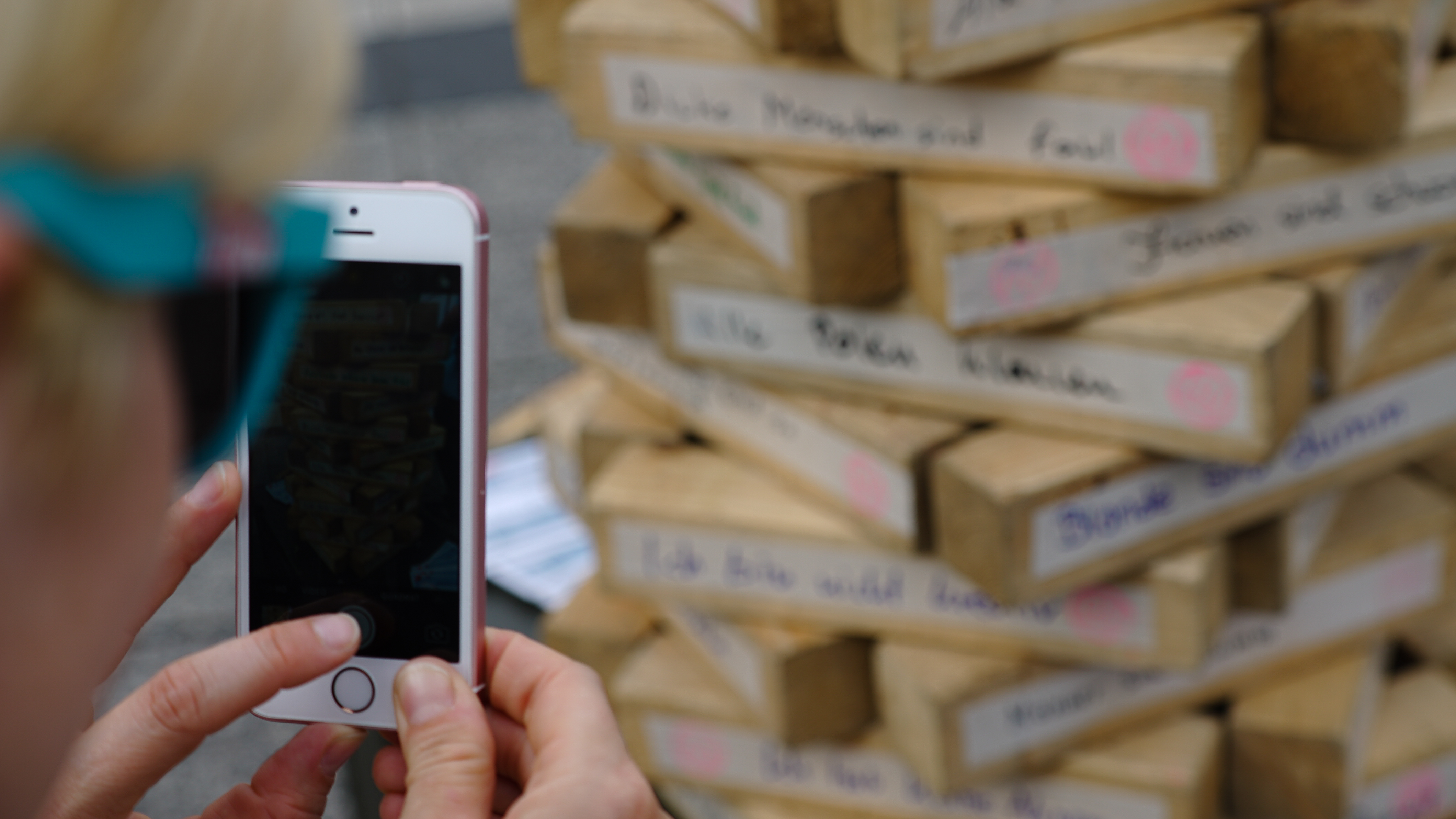 Ein Smartphone, das jemand benutzt, um ein Bild von dem Jenga Turm auf dem Albert-Magnus Platz zu machen.